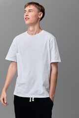 Fototapeta premium Man wearing a plain white tshirt in a minimal studio setup, relaxed pose with hands in pockets, focused expression, simple fashion and casual style for lifestyle clothing showcase