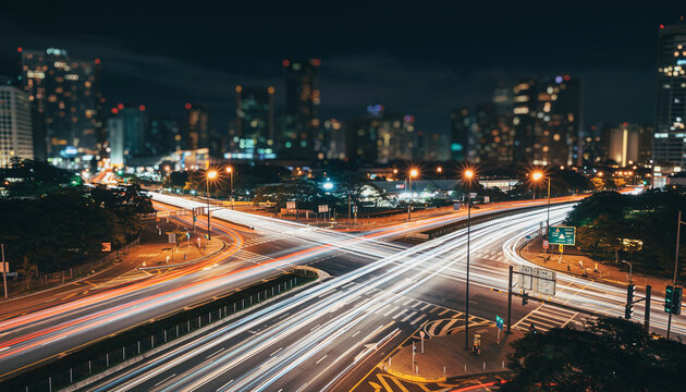 A Long-exposure Photograph Of A Busy City Intersection At Night, With Light Trails From The Traffic Creating A Sense Of Motion.