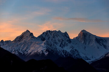 View of snow-capped jagged peaks under a soft, pastel sky, where the sun's gentle kiss paints the mountain tips with gold, Hunza, Gilgit Baltistan, Pakistan.