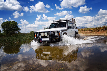 Off-road vehicle crossing shallow river in rural landscape © Jovan Vidaković
