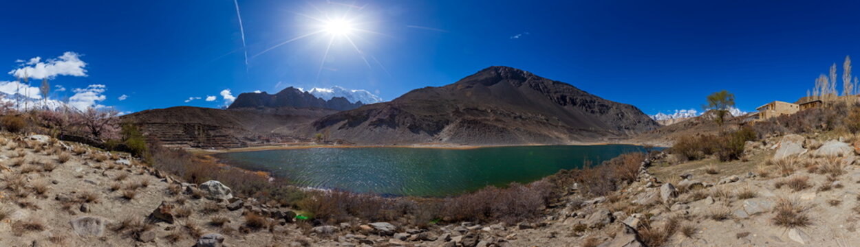 View of a serene lake mirroring the clear blue sky, framed by rugged mountains and sparse vegetation in the arid landscape, Hunza Nagar, Gilgit Baltistan, Pakistan.