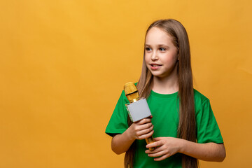 Happy pretty little girl in green t-shirt holding the microphone in her hands on yellow background. Child sings a song, speaks into a microphone, hosts a TV show, performs on the radio