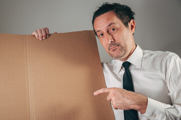 Businessman pointing at blank cardboard board, studio portrait with copy space, presentation, announcement, advertising, message, or communication concept.