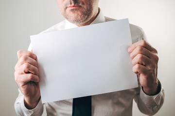 Serious businessman holding up blank white paper sheet mockup in office