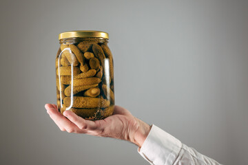 Hand holding glass jar of pickled gherkins cucumbers