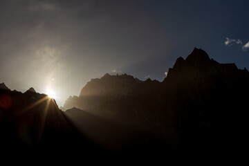 View of the sun's radiant fingers piercing through the rugged, silhouetted peaks, casting long shadows across the mountainous terrain, Passu, Gilgit Baltistan, Pakistan.