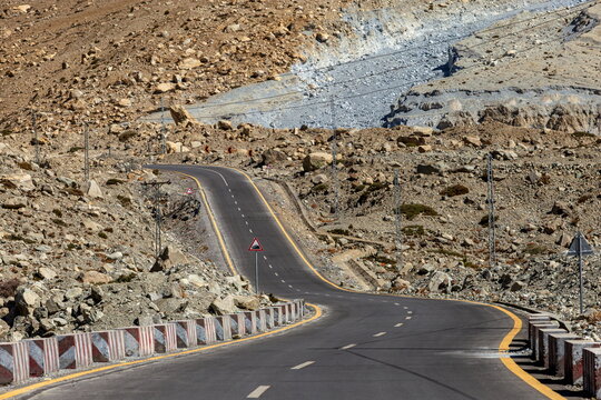View of the winding Karakoram Highway cuts through the rugged, rocky terrain under a vast sky, a ribbon of asphalt in the dramatic Passu, Gilgit Baltistan, Pakistan.