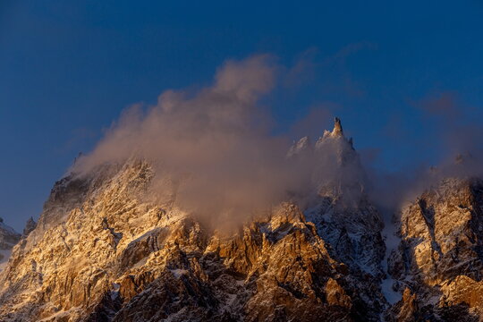View of the rugged, snow-dusted mountain peak piercing through ethereal clouds, kissed by the golden light of dawn in Passu, Gilgit Baltistan, Pakistan.