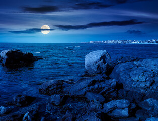 rocky shore of the sea coast under blue sky at night. beautiful view of coastal scene in full moon light. resort scenery during vacation season in summer. backdrop for fiction art or mystery concepts