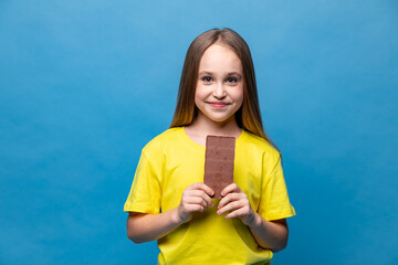 Cute little girl in yellow casual t-shirt holds chocolate bars on blue background, closeup. The concept of children's happiness and love for sweets. High quality photo. Copy space