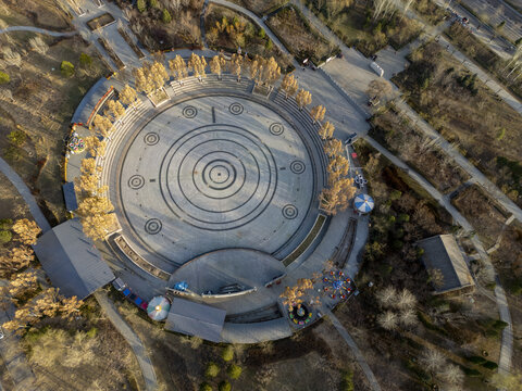 Aerial view of a circular plaza with concentric rings and radial lines creating a mesmerizing pattern, surrounded by golden trees and low buildings, Pingyao, Jinzhong, Shanxi, China.