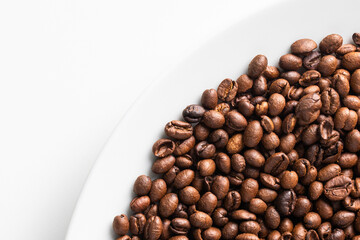 Top view of roasted coffee beans on the white plate, copy space
