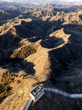 Aerial view of the snaking Great Wall of China, a stone dragon traversing rugged terrain under a golden sunset, Jingshanling, Beijing, China.