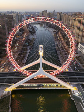 Aerial view of the Tianjin Eye Ferris wheel reflecting on the tranquil river, framed by urban architecture under a soft sky, Tianjin, Tianjin, China.