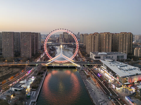 Aerial view of The Tientsin Eye Ferris wheel reflected in the river, framed by buildings under a pastel sky, Tianjin, Tianjin, China.