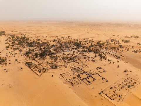 Aerial view of settlements nestled amidst the vast expanse of the desert, where ochre sands meet the horizon under a hazy sky, Mauritania, Mauritania.