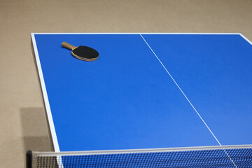 A blue ping pong table with a net and a racket