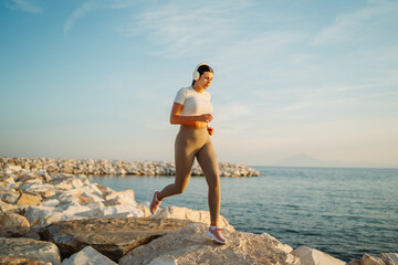 Woman running on rocky seashore wearing headphones