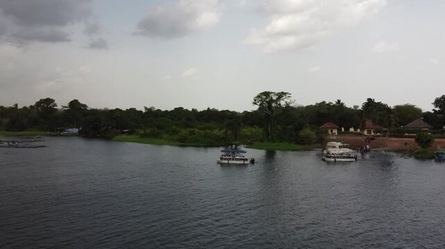 Aerial drone footage of Ghana, Africa, serene lake surrounded by mountains. Traditional boats across the water near a local village, with views near the Right to Dream Football Academy