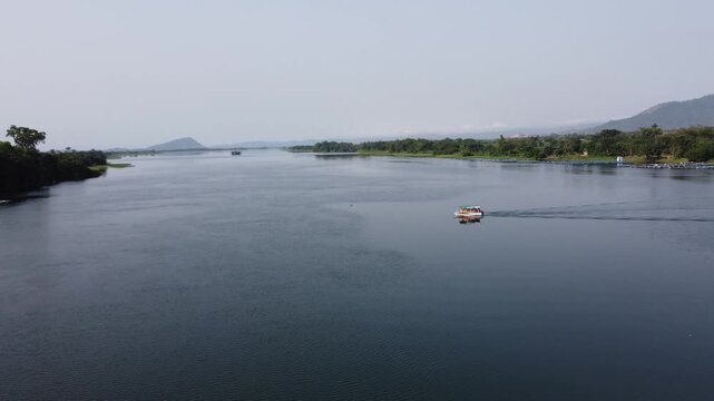 Aerial drone footage of Ghana, Africa, serene lake surrounded by mountains. Traditional boats across the water near a local village, with views near the Right to Dream Football Academy