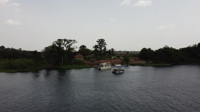 Aerial drone footage of Ghana, Africa, serene lake surrounded by mountains. Traditional boats across the water near a local village, with views near the Right to Dream Football Academy