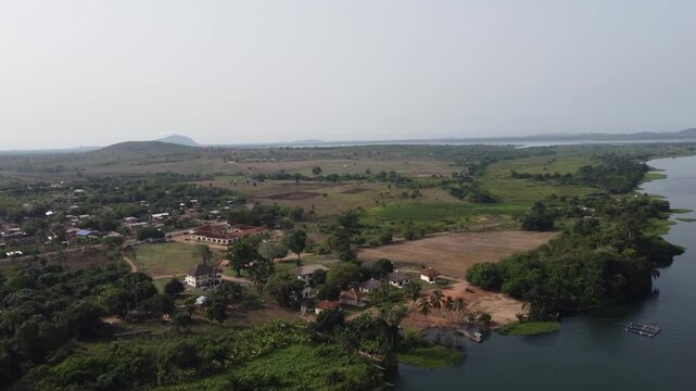Aerial drone footage of Ghana, Africa, serene lake surrounded by mountains. Traditional boats across the water near a local village, with views near the Right to Dream Football Academy
