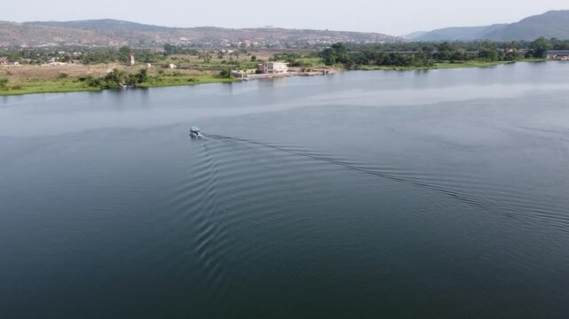 Aerial drone footage of Ghana, Africa, serene lake surrounded by mountains. Traditional boats across the water near a local village, with views near the Right to Dream Football Academy