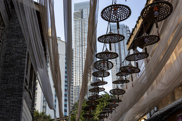 View of hanging woven lanterns casting shadows amidst draped white fabric with modern buildings towering in the background, Chongqing, Chongqing, China.