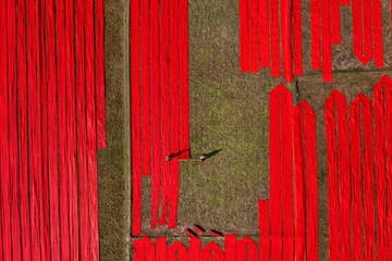 Aerial view of vibrant red fabrics spread across the landscape, contrasting sharply with the muted earth tones, Narsingdi, Dhaka Division, Bangladesh.