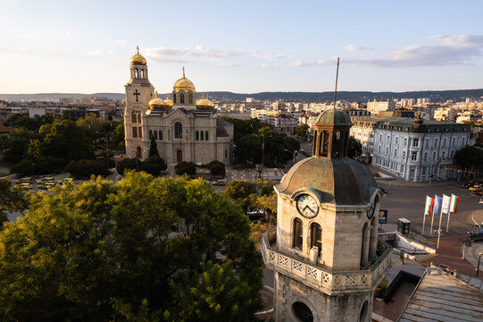 Aerial view of the golden domes of the Cathedral of the Assumption contrasting against the city's muted tones, with the clock tower standing tall, Varna, Bulgaria.