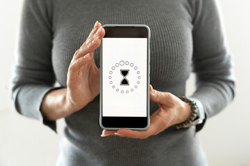 Girl Shows A Smartphone With A Loading Process And A Rotating Sandglass Icon On A White Screen