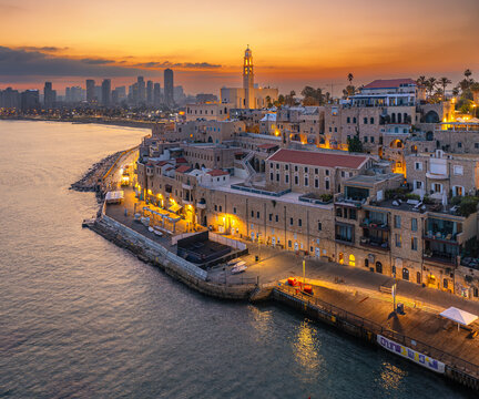 Aerial view of the ancient port city of Jaffa meeting the modern skyline of Tel Aviv under a fiery sunset, Tel Aviv-Yafo, Tel Aviv District, Israel.