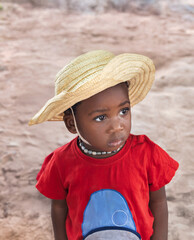 village african girl child, straw hat and red shirt, outdoors in the nature , sand ground