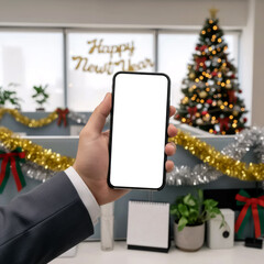 hand in a grey suit holding a smartphone with a white screen against a decorated tree in office