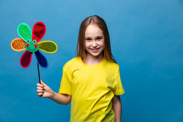 Photo of little cheerful girl in yellow t-shirt, happy positive smile child holds colorful paper toy windmill isolated over blue background. Summer vibes concept. Copy space. High quality photo