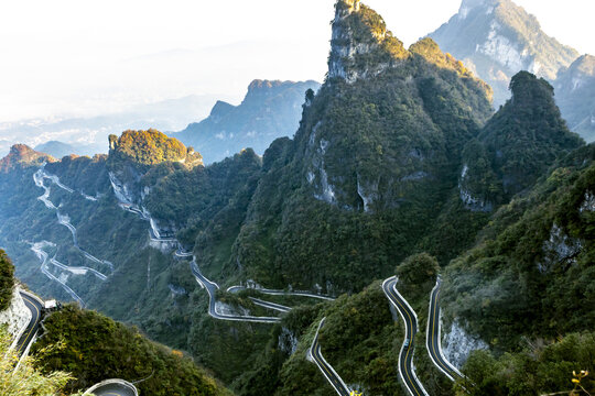 View of a winding mountain road snaking through lush green peaks under a bright sky, Zhangjiajie, Hunan, China.