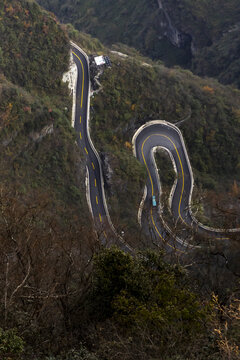 View of a winding road snakes through the lush, mountainous terrain, its sharp curves carving a path amidst vibrant greenery, Zhangjiajie, Hunan, China.