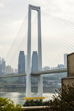 View of a modern white suspension bridge with thin cables stretches across the water connecting to tall buildings, Chongqing, Chongqing, China.