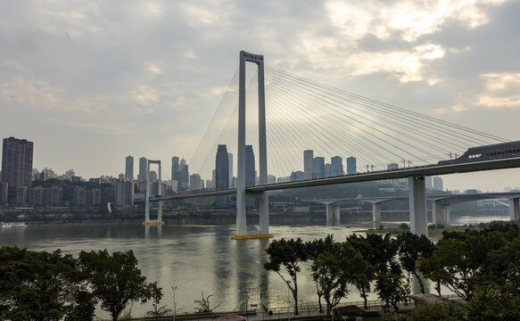 View of a modern suspension bridge stretches across the wide river, connecting the city skyline under a hazy sky, Chongqing, Chongqing, China.
