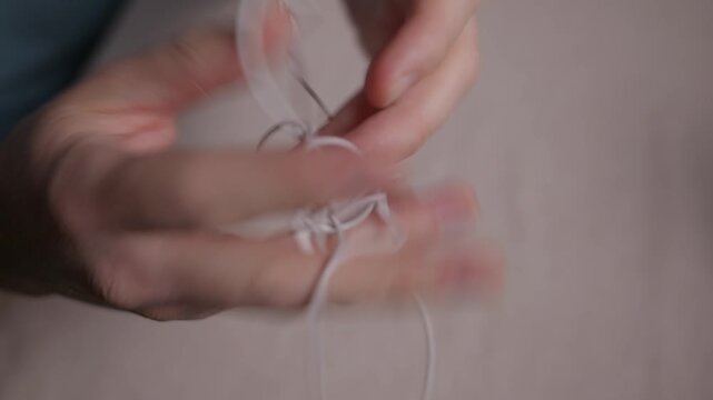 Close up of hands untangling wired earphones. Focus on cable movement and fingers without face, showing a common everyday problem and simple routine action. High quality 4k footage