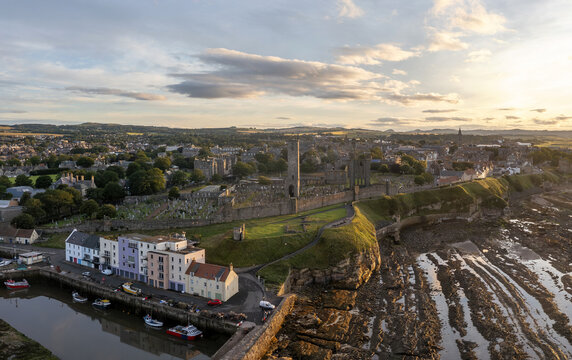 Aerial view of the ancient St Andrews Cathedral ruins rise majestically against the golden sunset, casting long shadows on the rugged coastline, St Andrews, Scotland, United Kingdom.