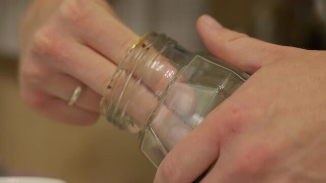 Close up of a spoon scooping instant coffee from a glass jar. Focus on hands and coffee granules without face, showing a calm everyday kitchen routine. High quality 4k footage