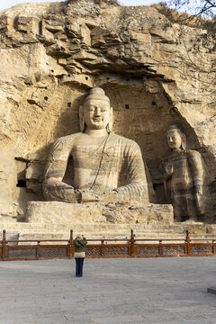 View of colossal sandstone Buddhas carved into cliffside, a testament to ancient artistry and spiritual devotion, bathed in the soft glow of daylight, Datong, Shanxi, China.