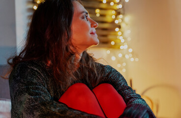 A young woman in red tights and a green sweater sitting at home against a backdrop of garland. Christmas and New Year holidays concept.