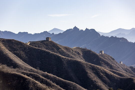 View of the Great Wall snaking across rugged, undulating hills under a hazy sky, ancient stone contrasting with the vast mountainous landscape, Chengde, Beijing, China.