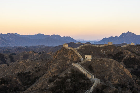 View of the ancient Great Wall snakes across rugged mountain peaks under a soft, fading sunset, a timeless monument in Jinshanling Great Wall Tourist Area, Chengde, China.