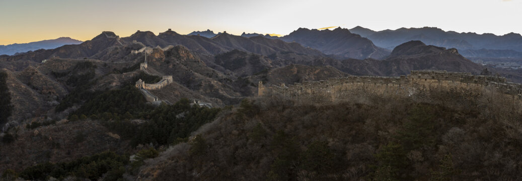 View of The Great Wall snaking across rugged terrain, a testament to history against the backdrop of distant mountains at sunset, Jinshanling, Chengde, China.