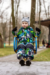 Five-year-old boy riding a swing in a winter park