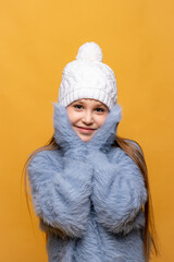 Child girl in a blue sweatshirt and white knitted hat with pompom on yellow background. Children emotions, joy and delight concept. Advertising clothing and sales. Ski resort vacation, copy space