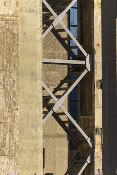 View of the crisscrossing metal beams contrast against the textured concrete, with a glimpse of blue window adding depth, Beijing, Beijing, China.
